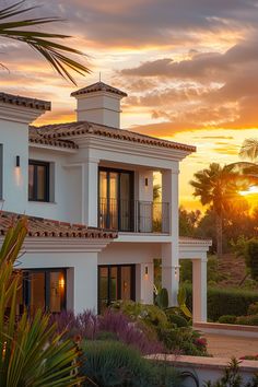 the sun is setting in front of a large house with balconies and palm trees