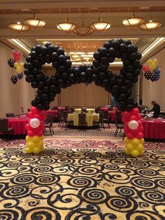 mickey mouse balloon arch in the middle of a banquet hall decorated with black, yellow and red balloons