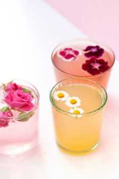 three glasses filled with water and flowers on top of a white table next to each other