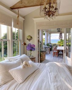 a bedroom with a bed, chandelier and large windows overlooking the outdoors area