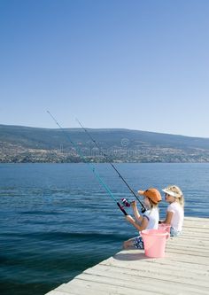 two women sitting on a dock with fishing rods in their hands royalty images and stock photos