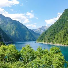 a lake surrounded by mountains and trees in the foreground with blue water on either side