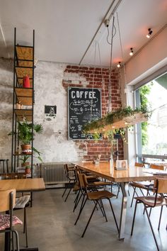 the interior of a coffee shop with tables, chairs and plants hanging from the ceiling