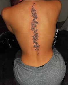 the back of a woman's lower back tattoo with flowers and leaves on it