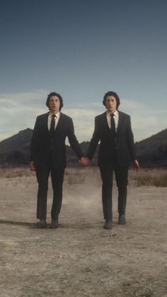 two men in suits holding hands and walking through the desert