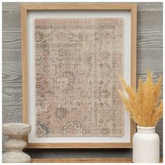 an old rug is displayed in front of a white vase with some dried flowers on it