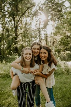 three girls hugging each other while standing in the grass with their arms around one another