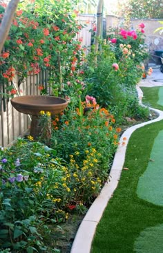 a garden filled with lots of flowers next to a fence and green grass covered ground