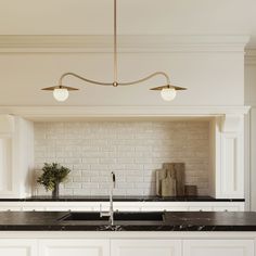 a kitchen with white cabinets and black counter tops, two lights above the sink are brass fixtures