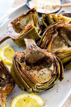 grilled artichokes on a plate with lemon wedges