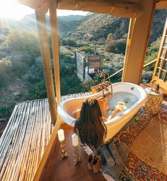 a woman is sitting in the bathtub with her feet on the floor and looking out over the valley