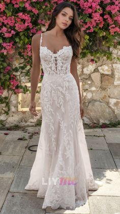 a woman in a white wedding dress standing on a stone walkway with pink flowers behind her