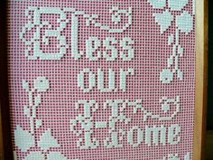 a cross - stitch pattern with words and flowers in white on pink background, framed by wooden frame