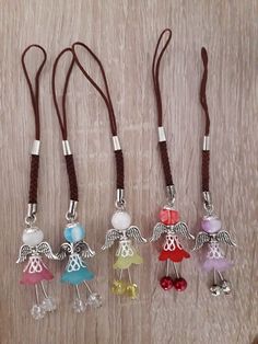 four little angel charms are hanging from brown cords on a wooden surface with beads and cord