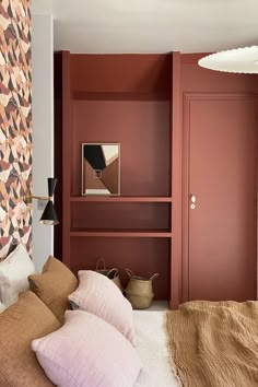 a bedroom with red walls and pillows on the bed, along with a bookcase