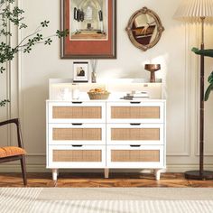 a white dresser sitting in a living room next to a chair and potted plant