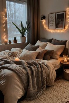 a bed with blankets, pillows and candles in front of a window filled with lights