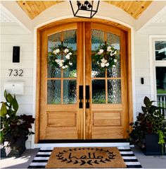 a front door with two wreaths and flowers on the glass windows, next to a black and white checkered rug