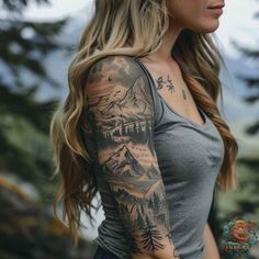 a woman with long blonde hair wearing a grey shirt and tattoos on her arm, standing in front of mountains