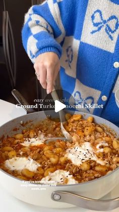 a person in a blue and white sweater is stirring food into a pan with a spoon