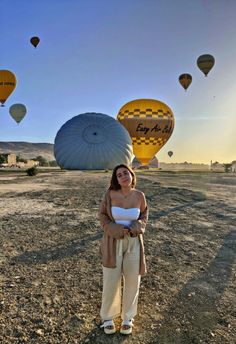 a woman standing in the middle of a field with hot air balloons flying above her