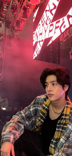 a young man sitting down in front of a neon sign