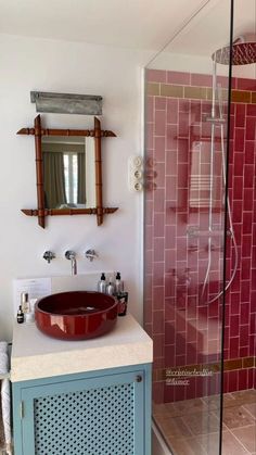 a bathroom with a sink, mirror and shower in it's stall area that has red tiles on the walls