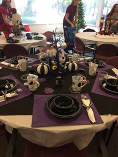 the table is set with black and white plates, silverware, and purple napkins