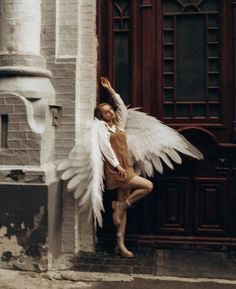 a woman with white wings standing in front of a door and holding her arm up