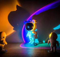 three small toy figures standing next to each other in front of a colorful light background