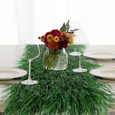 an arrangement of flowers and greenery in a vase on a table with wine glasses