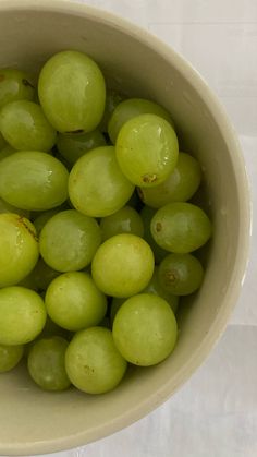 a bowl filled with green grapes on top of a white tablecloth covered flooring