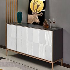 a white and black cabinet with a deer painting on it's sideboard next to two wine glasses