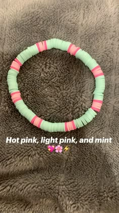 a bracelet with pink and green strips on it, sitting on a gray blanket that says hot