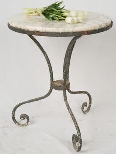 a marble topped table with wrought iron legs and flowers on top, against a white background