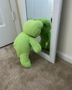 a large green teddy bear standing in front of a mirror with its head on it's back