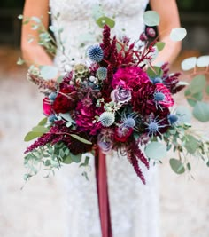 a bridal holding a bouquet of red flowers and greenery in her hands,