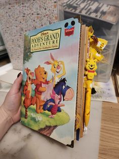 a winnie the pooh book is being held up by a person's hand