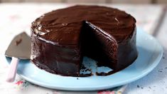 a chocolate cake on a blue plate with one slice taken from it and the rest of the cake in the background