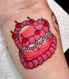 a pink cake with cherries and pearls on the side of her left arm is shown