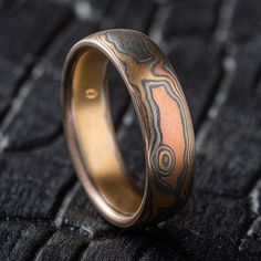 "* Price may vary depending on ring size, please inquire with us directly with your needed size for accurate pricing! This unique Mokume Gane band is shown in the Woodgrain pattern and the Firestorm metal combination, with a low dome profile, and an etched and oxidized finish. Firestorm features 14k red gold, 14k yellow gold, Palladium, and sterling silver.   Pattern: Woodgrain Palette: Firestorm  Finish: Etched and Oxidized Profile: Low Dome Width Shown: 6mm Size Shown: 9.25 Price does NOT include stones or setting fees. We care about customer service and would like to hear from you! Please contact us to help create your treasured item, we take your concerns and requests to heart and will work together to create your unique designs SPECIAL PRICING FOR SETS. CONTACT US WITH YOUR DESIRED WI Round Patina Rings For Anniversary, Adjustable Hand Forged Fusion Rings, Artisan Promise Ring, Adjustable Patina Jewelry For Anniversary, Artisan Rings With Patina And Adjustable Fit, Artisan Patina Rings For Anniversary, Artisan Adjustable Yellow Gold Ring, Mokume Gane Ring, Titanium Rings For Men