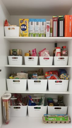 an organized pantry with white bins filled with books and other items on the shelves