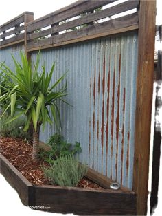 a wooden planter filled with lots of plants next to a metal wall and fence