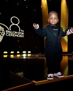 a young boy in a tuxedo standing on stage with his hands out to the side