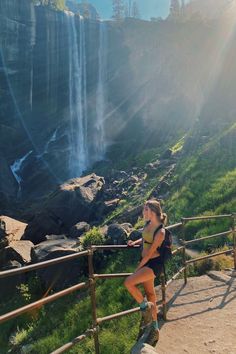 a woman standing on the side of a wooden railing in front of a large waterfall