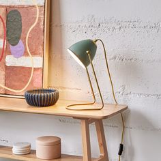 a wooden shelf with a lamp on it next to a white brick wall and a painting