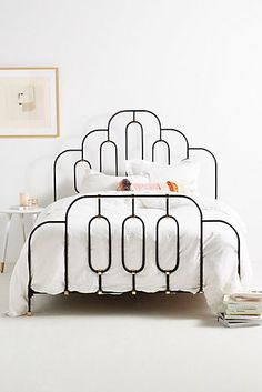 a white bed with black iron frame and pillows on top of it in a bedroom