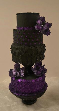 a three tiered cake with purple flowers on the top and black icing around it