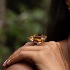 The Story Bright and bold, this vintage cocktail ring from the Retro era is a gorgeous piece. Done in warm 14 karat yellow gold, the ring has an allover glow. At center is an extra-large emerald cut citrine weighing approximately 55 carats. The hand-cut stone sits in a four-prong setting made for the piece. On either side are four ruby cabochons that look like juicy pomegranates seeds. Moving down the band are six vintage single cut diamonds set in 14k white gold giving a sparkle filled finishin Citrine Cocktail Ring, Yellow Gemstone Jewelry, Smokey Topaz Ring, Retro Era, Yellow Style, Vintage Cocktail Ring, Jewelry Staples, Smokey Topaz, Silver Gold Jewelry