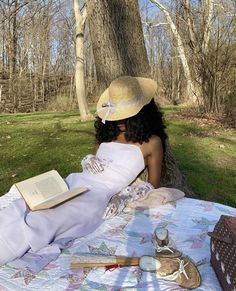 a woman is sitting on the grass reading a book while wearing a hat and dress